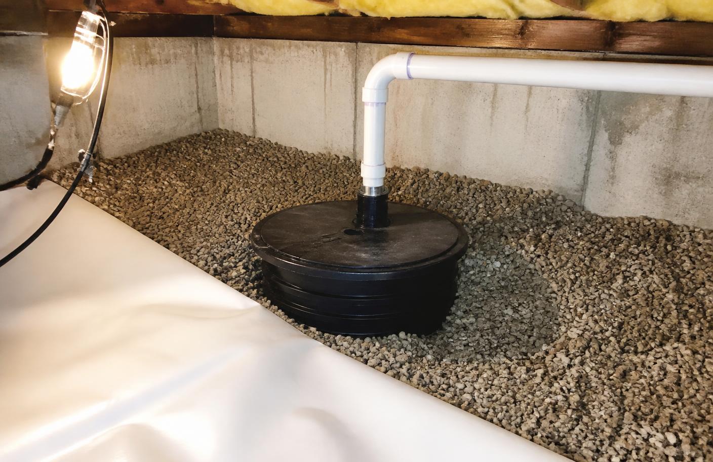 Sump pump basin and discharge pipe installed in a gravel bed inside a crawl space